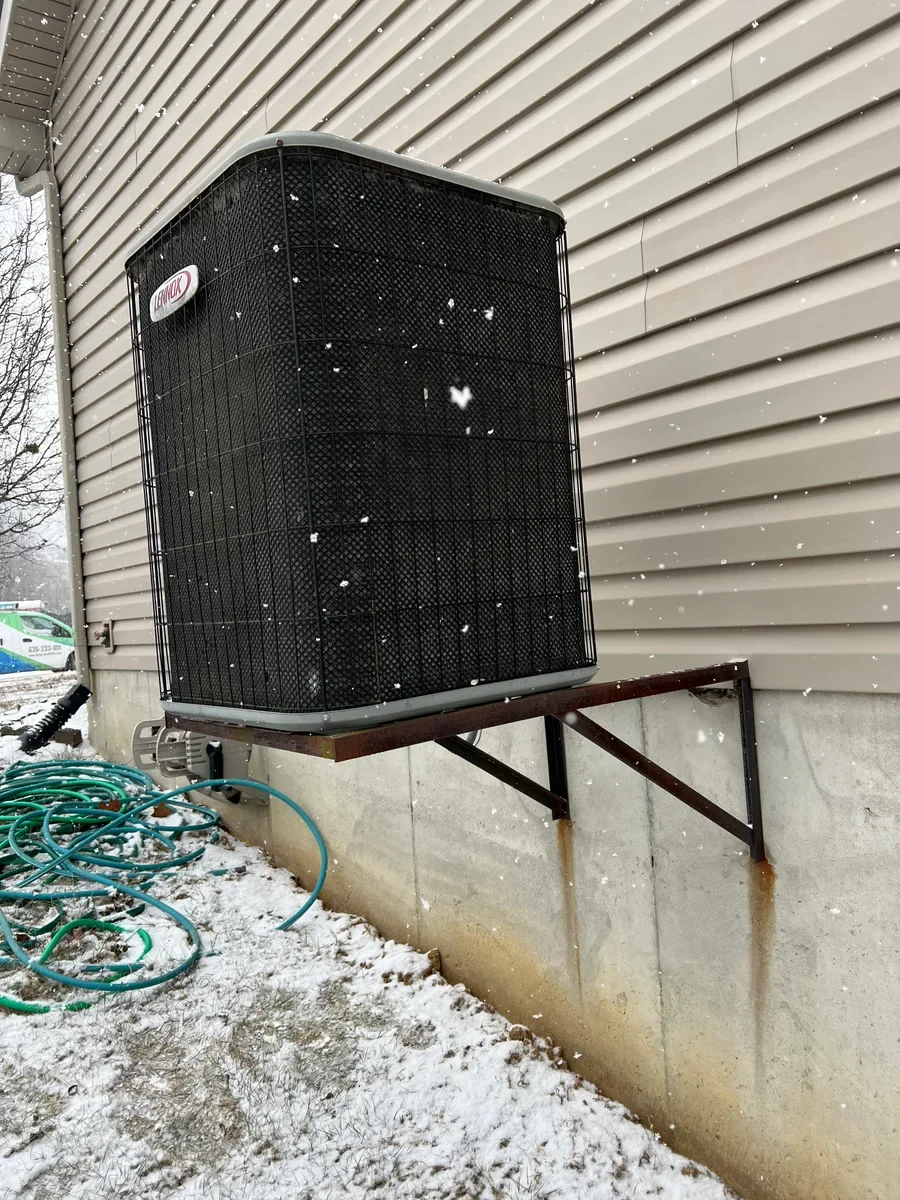Original air conditioner on a wall bracket before replacement in O'Fallon.